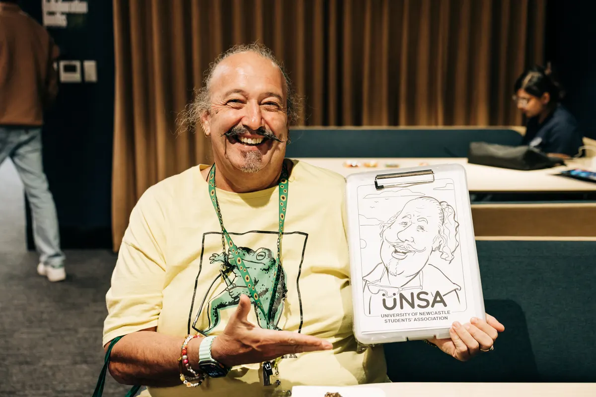Man with a moustache smiling, holding his caricature with the UNSA university logo