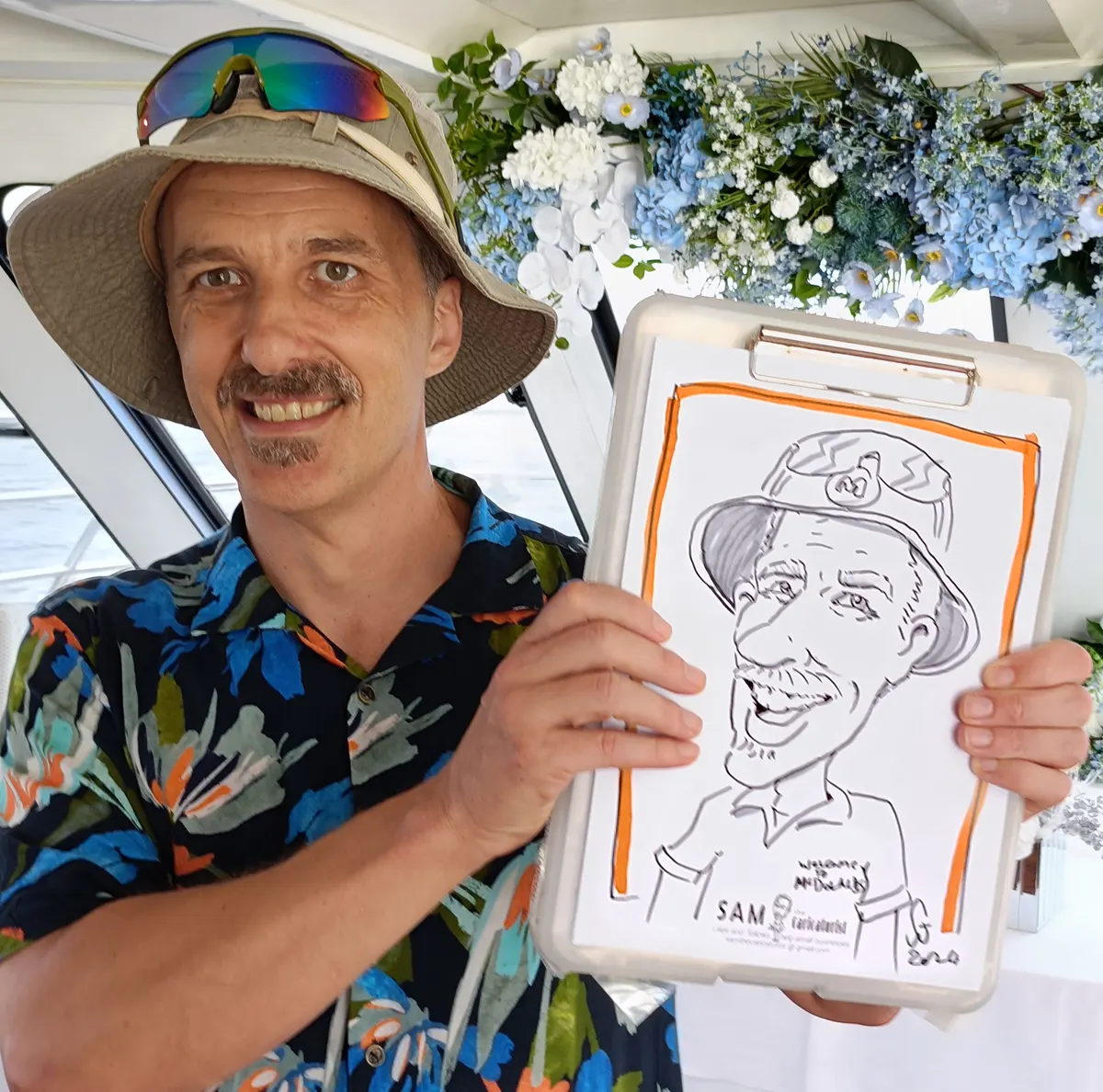 Man in a bucket hat holding his caricature on a clipboard